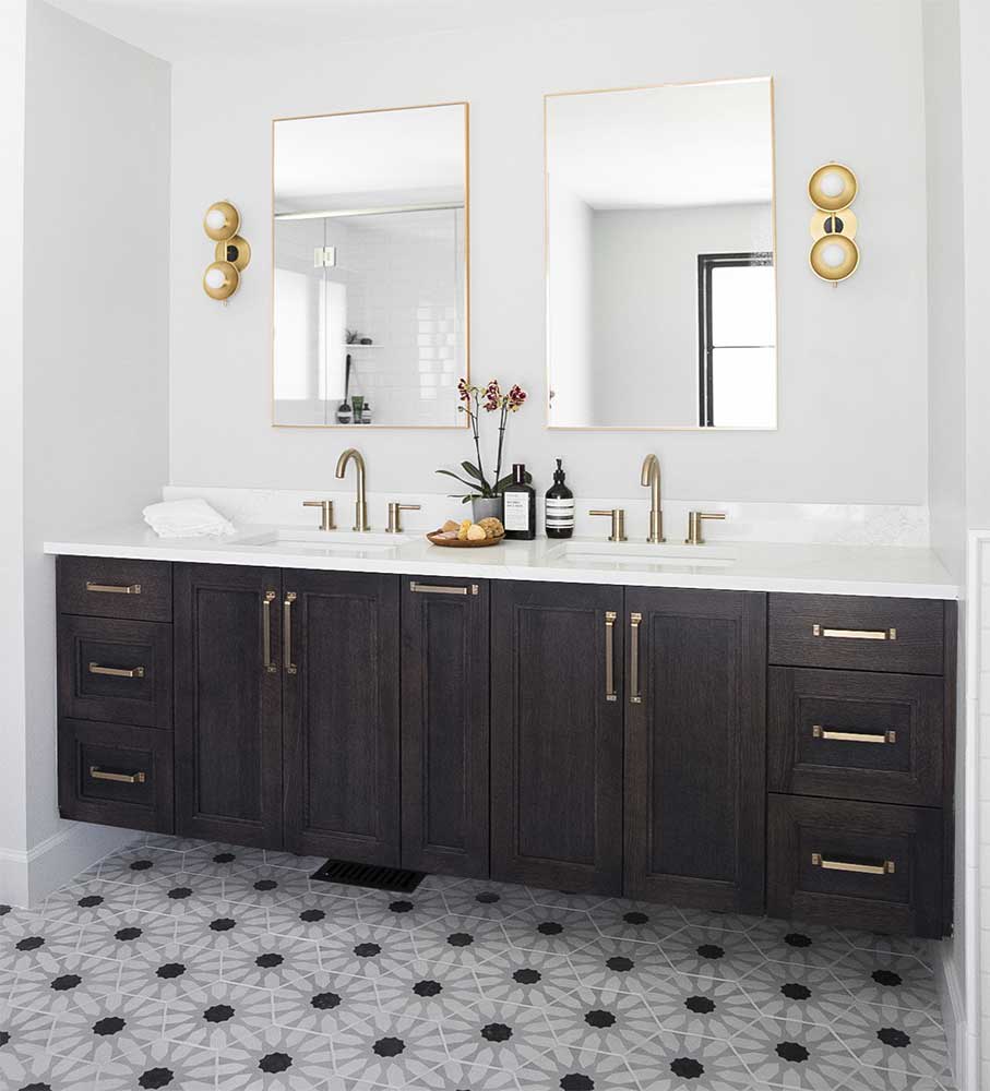 Bathroom with a dark wood double vanity, twin brass-framed mirrors and sconces above black and white patterned floor tile