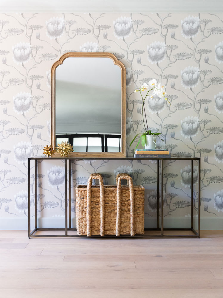 Hallway console table with an arched gold mirror against floral wallpaper, styled with woven baskets and an orchid