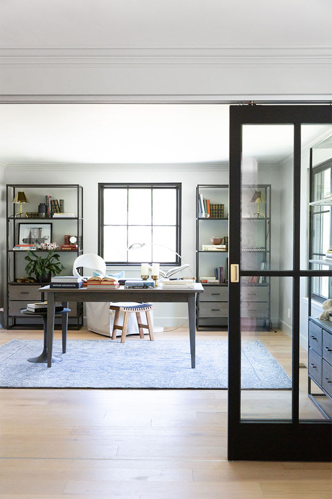 Home office framed by a black steel-and-glass pocket door, with a white desk between black shelving units