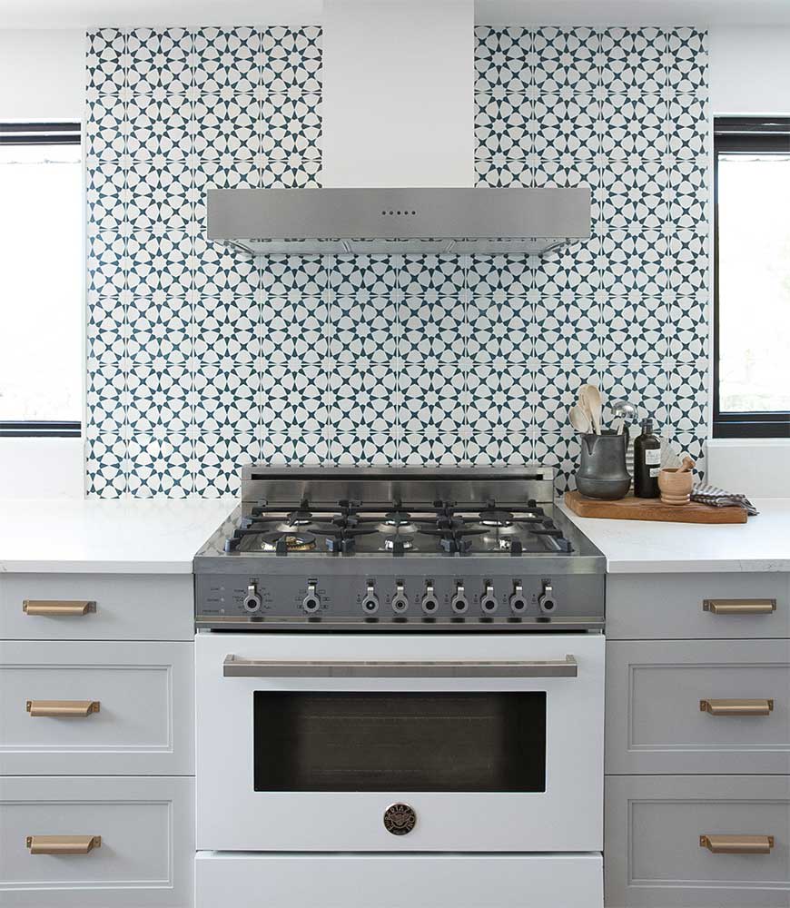 White range with brass trim under a stainless hood, against a blue and white star-patterned tile backsplash