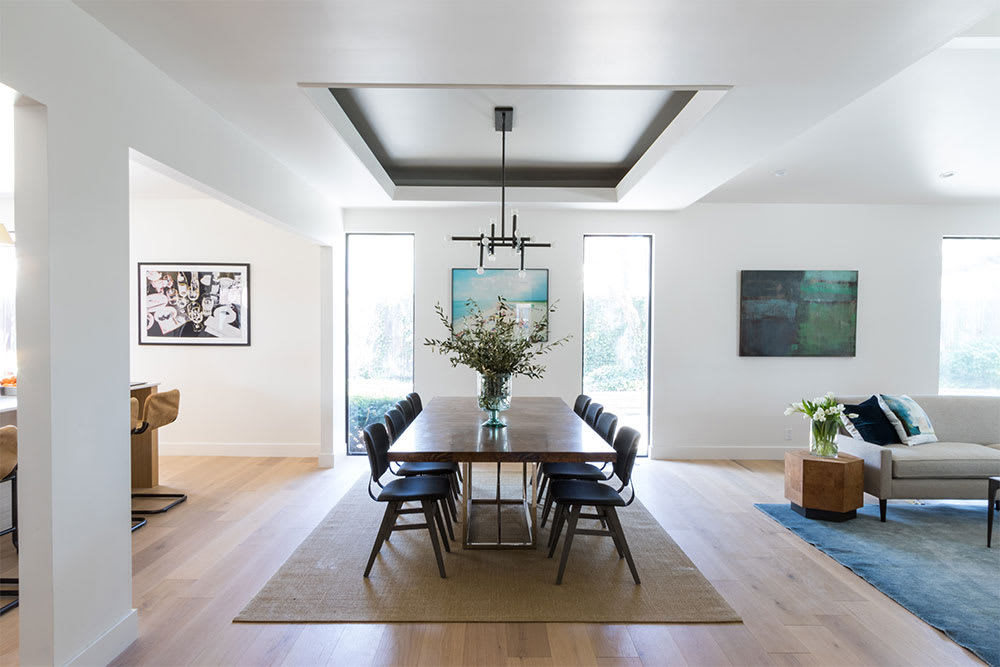 Dining table with black chairs beneath a linear pendant set into a recessed ceiling panel