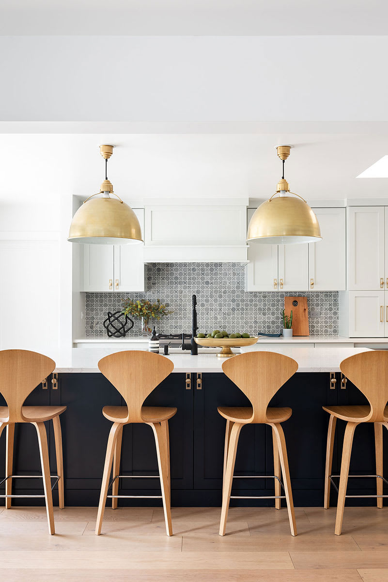Navy kitchen island with bentwood barstools under oversized brass dome pendants, against a grey patterned tile backsplash