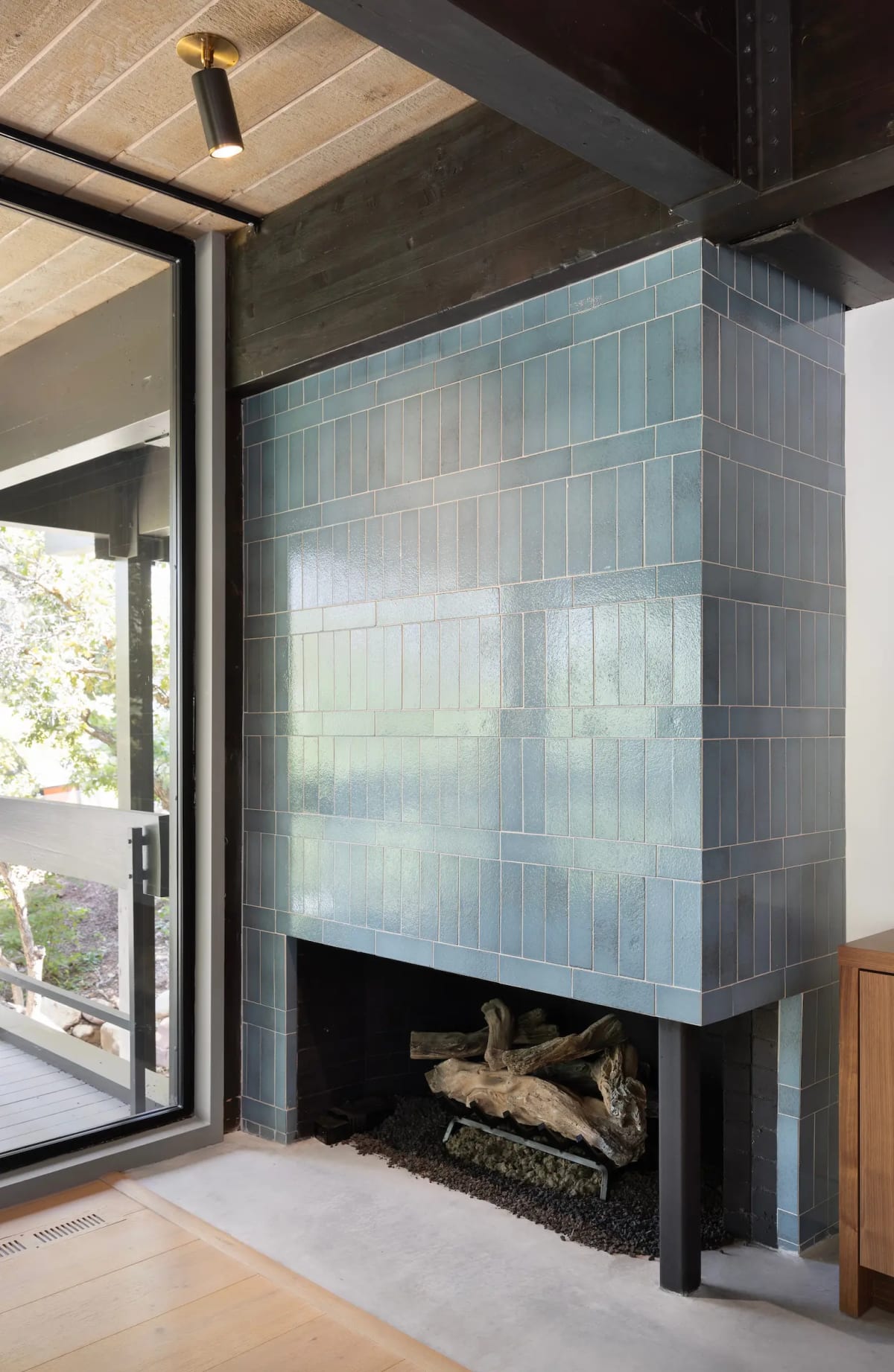 Floor-to-ceiling fireplace clad in blue-green glazed tile, stacked with driftwood beside a glass door to the deck