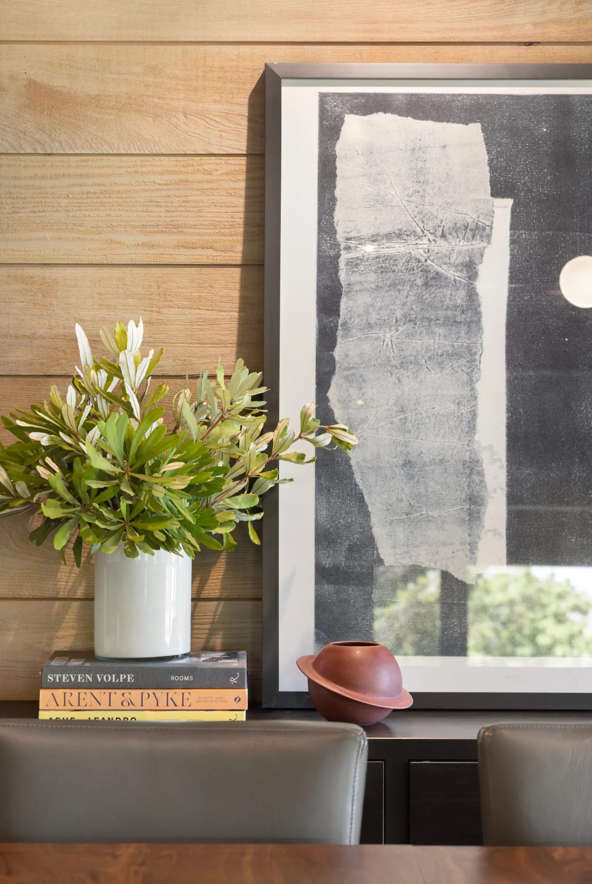 Styled vignette of foliage in a white vase on stacked design books beside a framed black and white abstract print