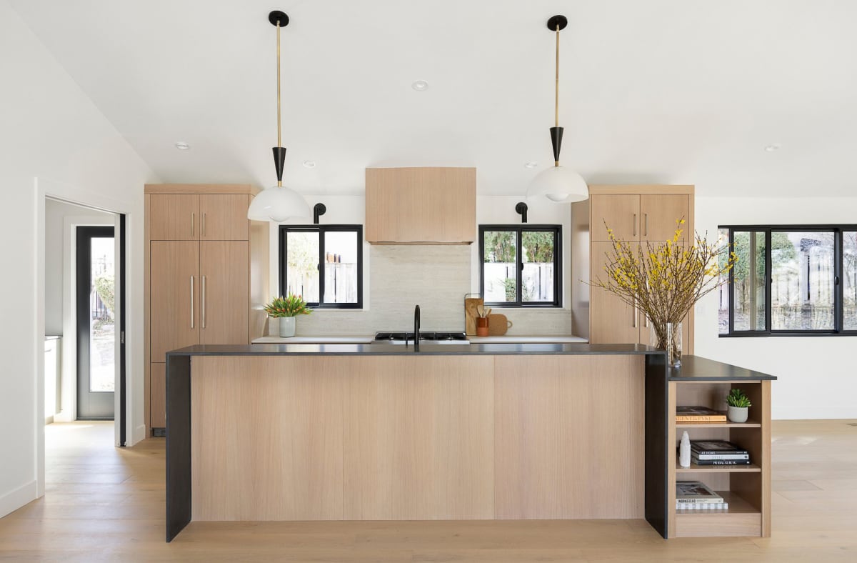 White oak kitchen island with a black stone counter under black and white pendant lighting