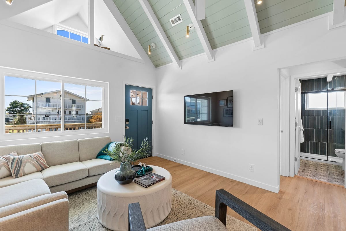 Living room with a teal front door, vaulted seafoam plank ceiling and a cream sectional facing a wall-mounted television