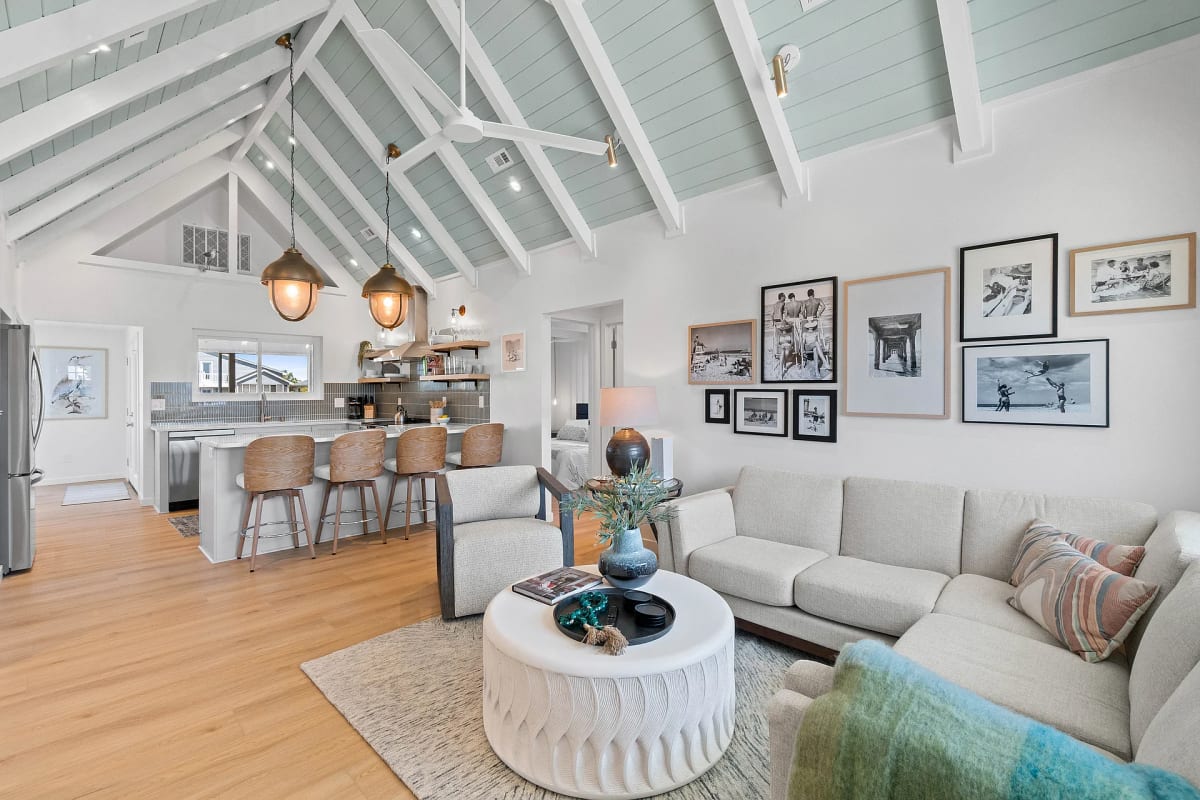 Open living and kitchen area under a vaulted seafoam ceiling, with a cream sectional, round ottoman and gallery wall
