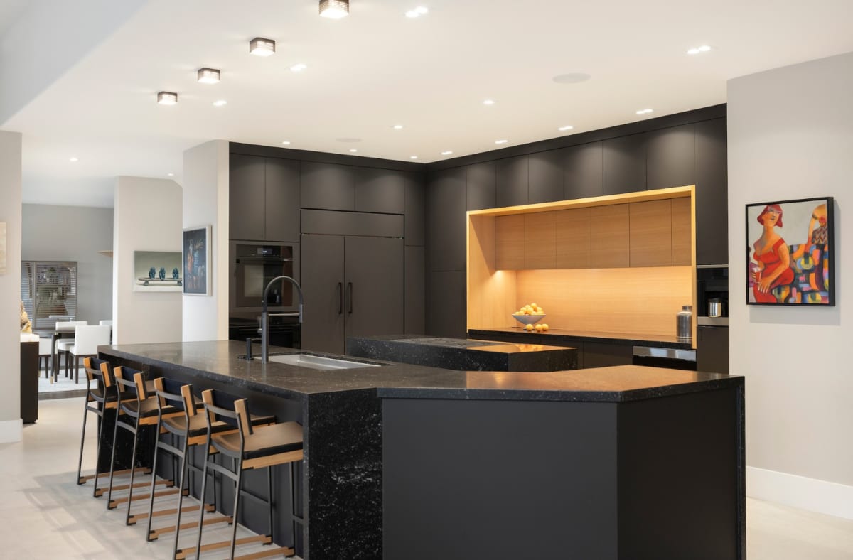 Dramatic black kitchen with a speckled granite island, leather barstools and a backlit white oak alcove