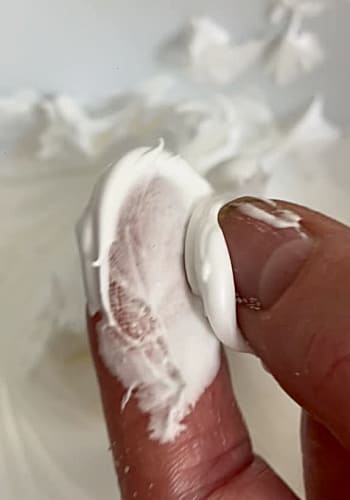 Meringue being rubbed between finger and thumb.