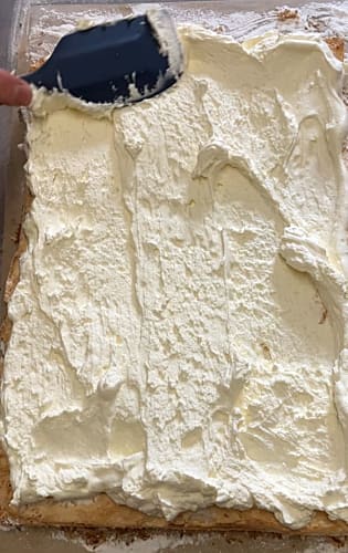 Whipped cream being spread evenly onto the roulade with a spatula.