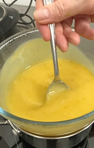 Spoon being held in the whisked lime curd mixture showing that it has thickened.