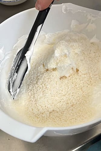 Dried coconut added to bowl of meringue.