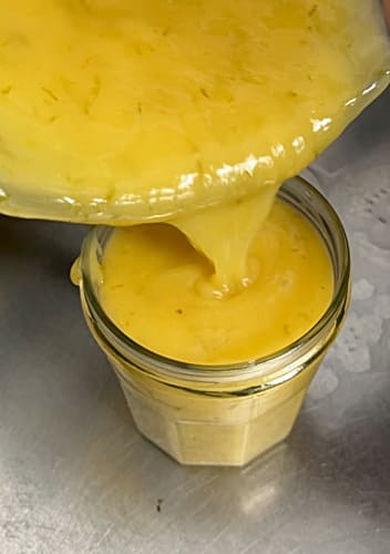 Lime curd being poured into a jam jar.