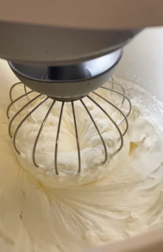 Cream being whisked with icing sugar showing soft peaks.