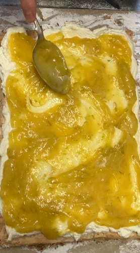 Lime curd being spread with a spoon onto the top of the whipped cream on the roulade.