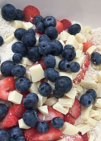 Fresh blueberries, strawberries and white chocolate chunks on top of the flour mixture in a bowl
