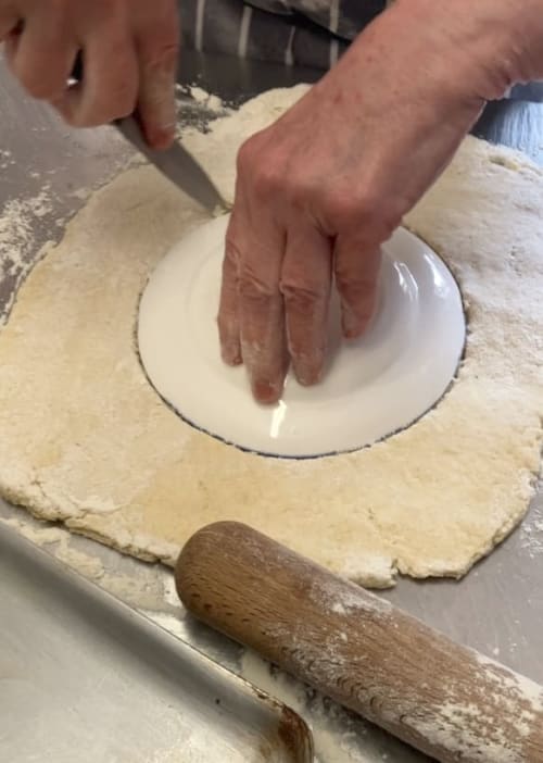 Small plate being used to cut out a circle of dough.