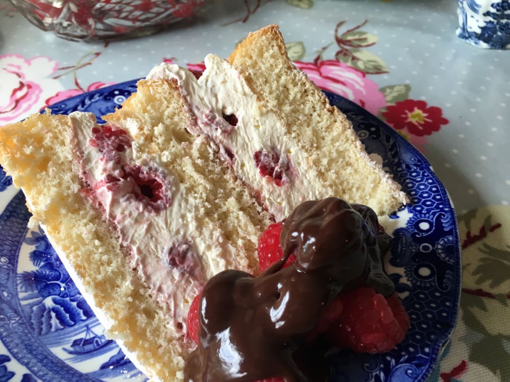 Slice of raspberry cream sponge served with fresh raspberries and a chocolate sauce