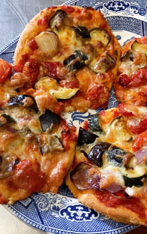 Four baked roasted Mediterranean vegetable pizzas on a blue plate.