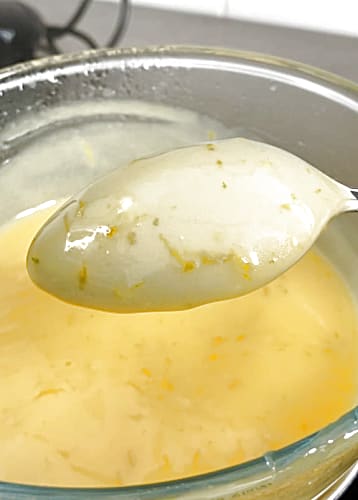 Lime curd coated onto the back of a spoon being held above the bowl of lime curd.