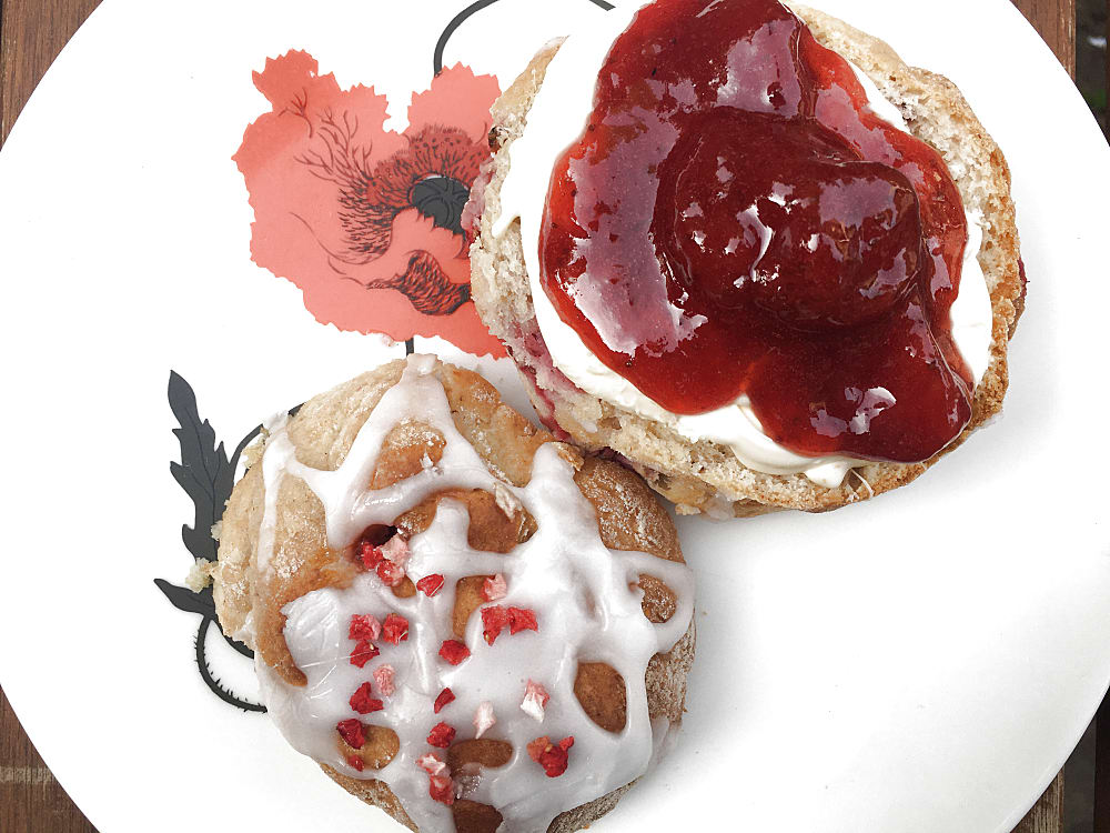 Strawberry and Rose scone cut in half on a plate with rose icing and strawberry sprinkles and spread with clotted cream and strawberry jam.