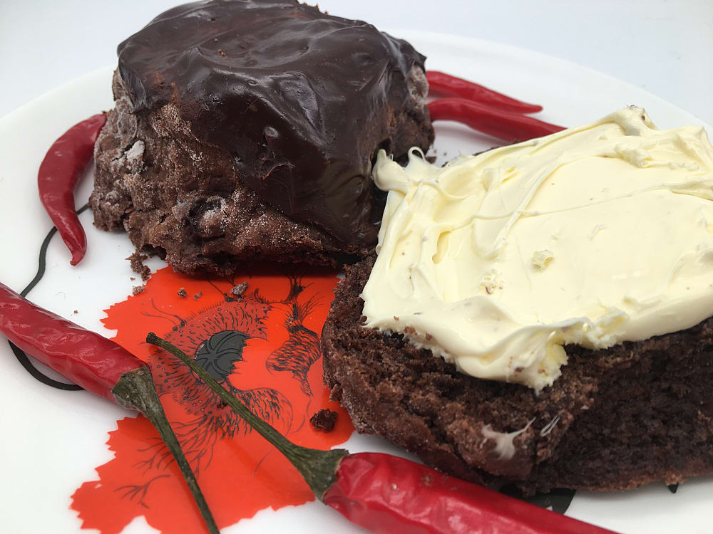 Chili chocolate scone cut in half with clotted cream spread on one half and chillies scattered on the plate