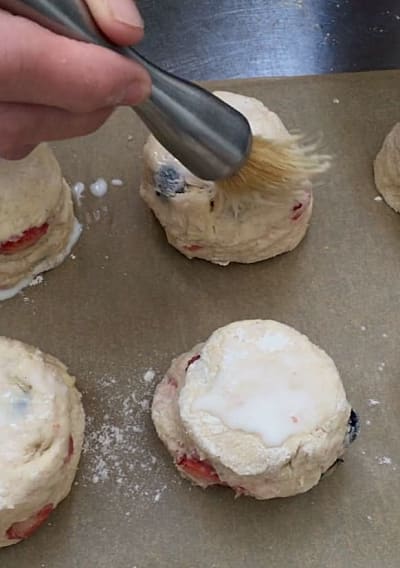 Milk being brushed onto the top of the uncooked scones