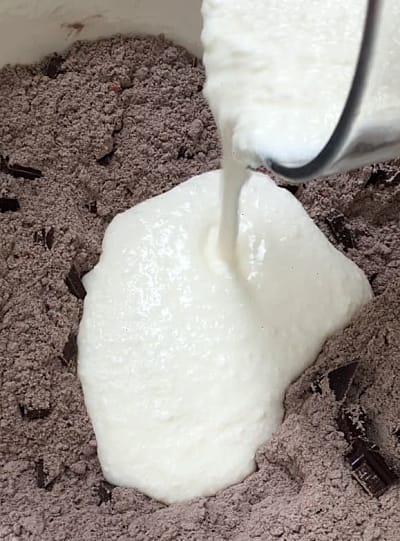 Buttermilk being poured into the flour and chocolate chunk mixture