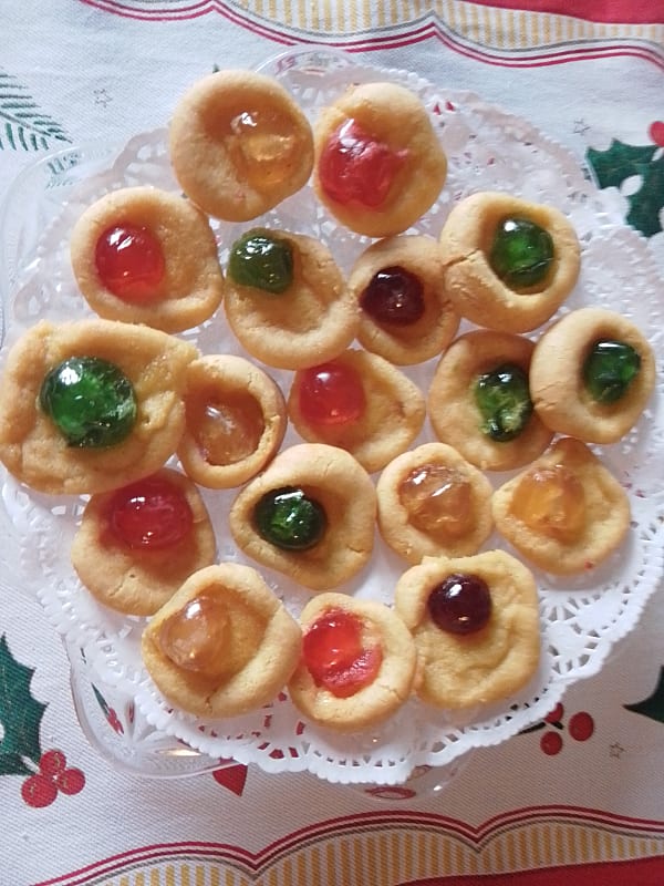 Little rounds of marzipan with red, yellow and green glacé cherries on a plate.