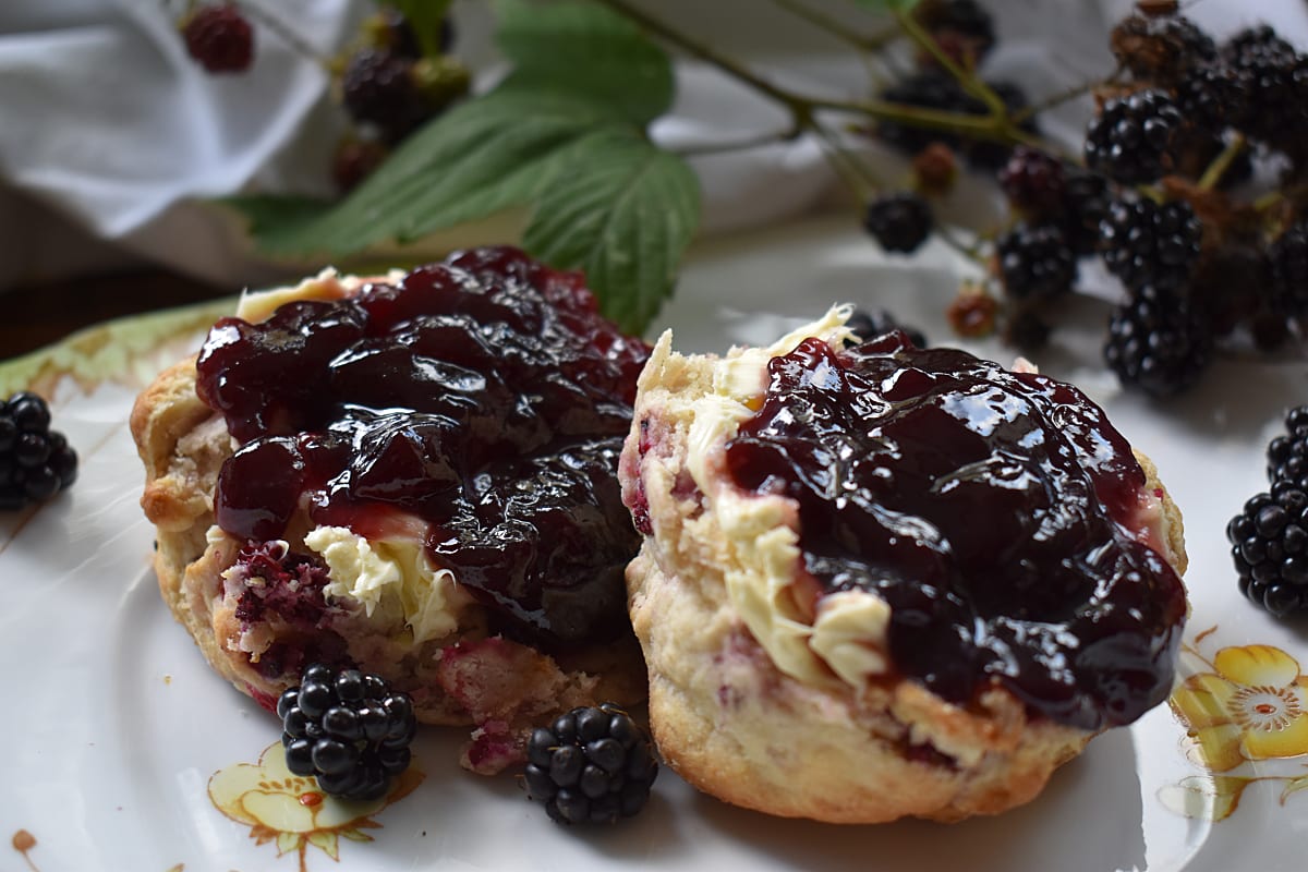 Apple and Blackberry Scones cut in half and spread with clotted cream and Bramley Preserve with wild blackberries scattered on the plate.