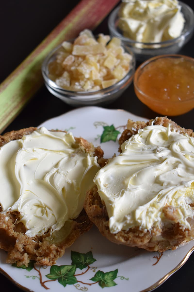 Rhubarb and Ginger Scones cut in half spread with clotted cream with dish of ginger preserve in background
