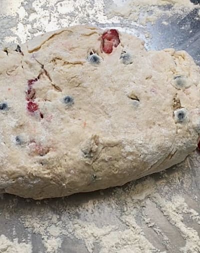 Dough mixed with strawberries, blueberries and white chocolate chunks on a floured work surface and