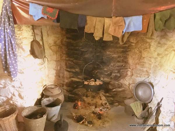A fire burning in a hearth with a pot hanging over it and clothes drying on a line.