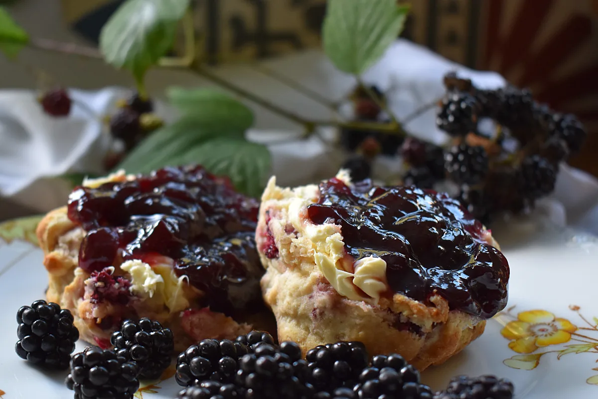 Apple and Blackberry Scones cut in half and spread with clotted cream and Bramley Preserve with wild blackberries scattered on the plate.