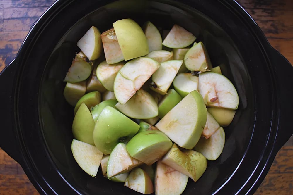 Apples cut into chunks in a slow cooker before cooking