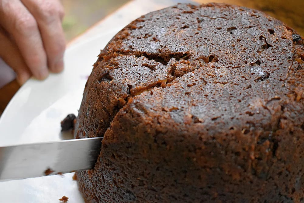Slice being cut from a whole Halloween Pudding with a knife on a white plate