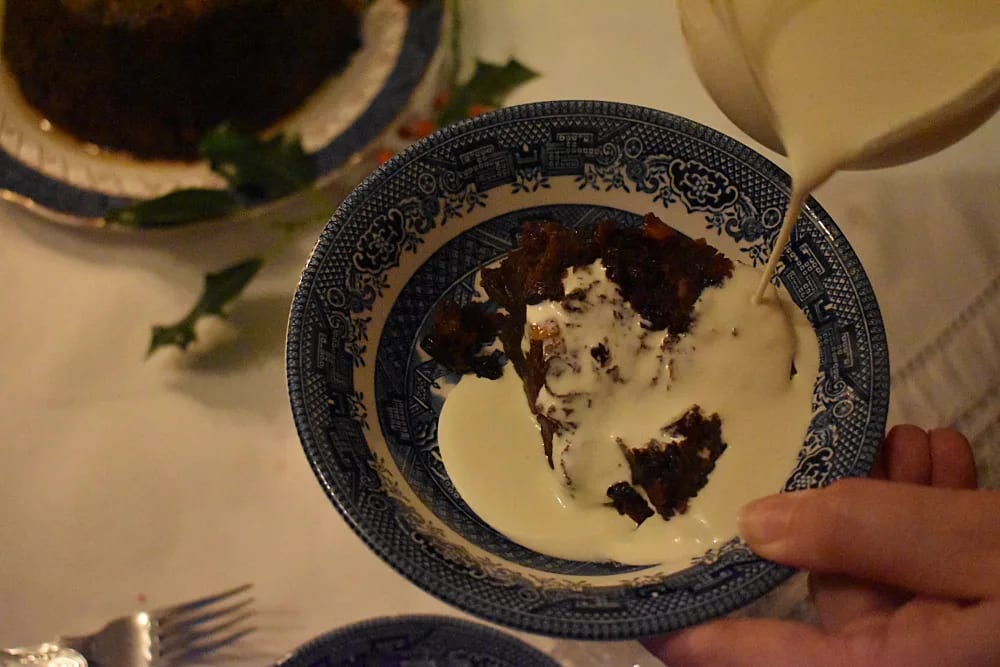 Slice of Christmas Pudding with cream being poured on it