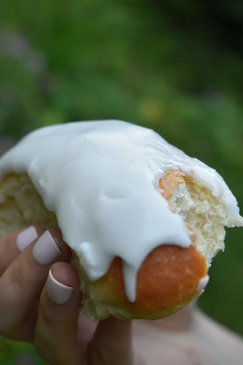 Iced bun with a bite taken out of it and held in a hand.