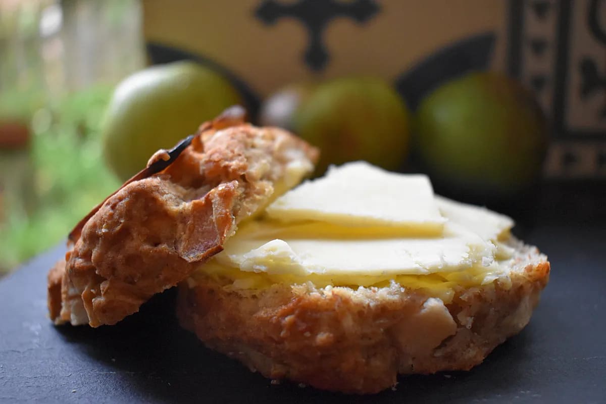 Apple and Cheese Scone cut in half, buttered with cheddar cheese and on a black board with apples in the background.