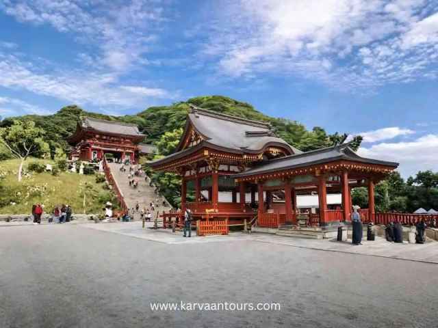 Visitors walking up stone steps between traditional red shrine buildings in Kamakura Japan
