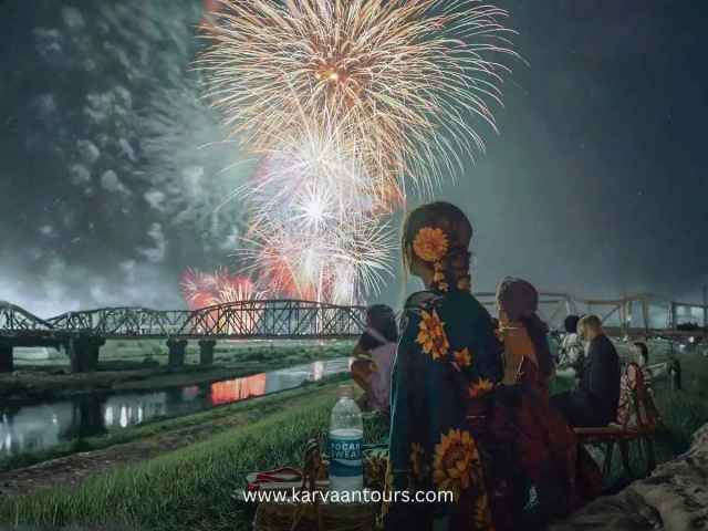 People in yukata watching a fireworks festival by the riverside in Japan at night