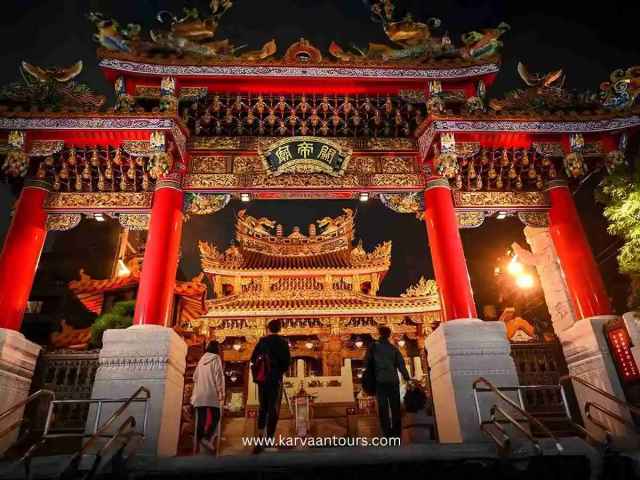Illuminated Yokohama Chinatown entrance gate at night with visitors walking toward the temple