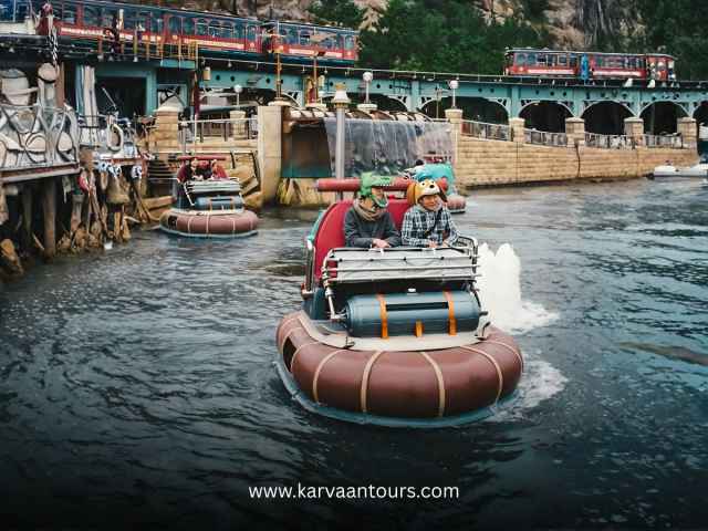 Tourists enjoying the Aquatopia water ride at Tokyo DisneySea with the electric railway passing in the background.