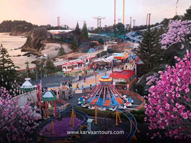 Aerial view of a seaside amusement park in Japan featuring classic carnival rides and scenic coastal cliffs at sunset.