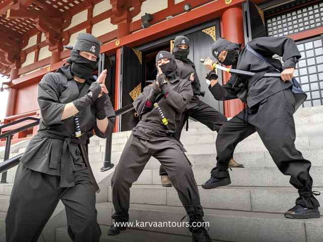 Group of performers dressed in traditional black Ninja outfits posing at a historic Japanese temple site.