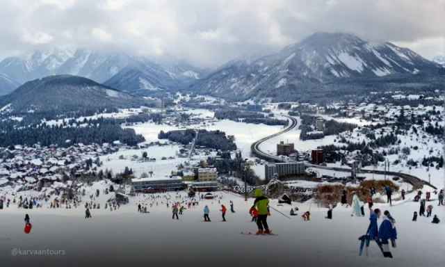 High-angle shot of a busy ski resort nestled in a snow-covered valley with mountains behind.