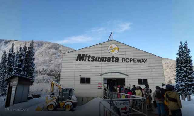 People lining up outside the Mitsumata Ropeway station building with snowy hills in the background.