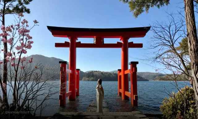 Red torii gate standing in Lake Ashi with visitor admiring the view in Hakone, Japan