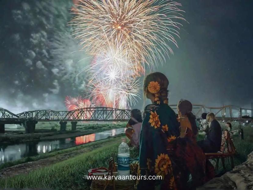 People in yukata watching a fireworks festival by the riverside in Japan at night