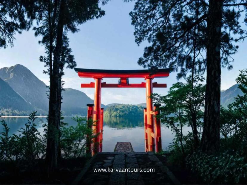Red torii gate of Hakone Shrine standing by Lake Ashi surrounded by trees and calm water scenery